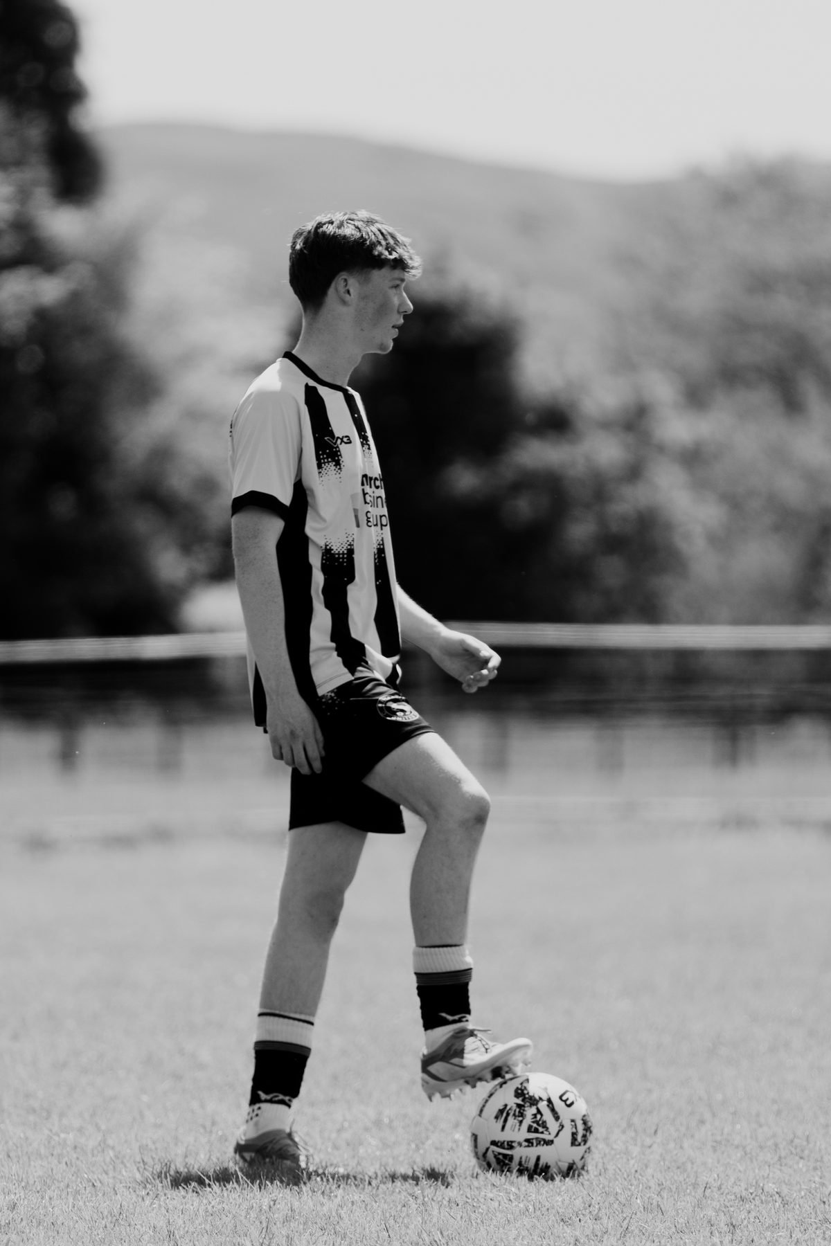 Young player resting a foot on the ball waiting for play to restart