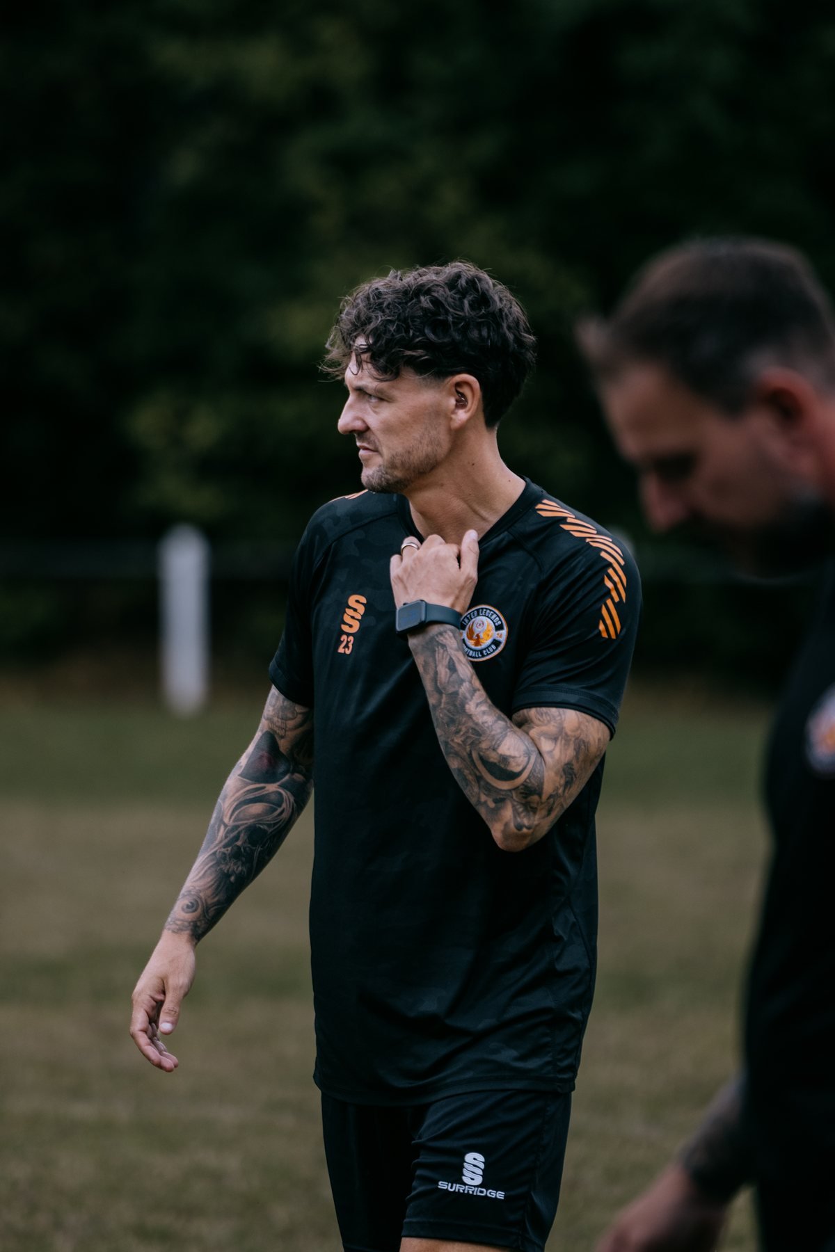 Player in a black and orange training top adjusting his collar during an evening session